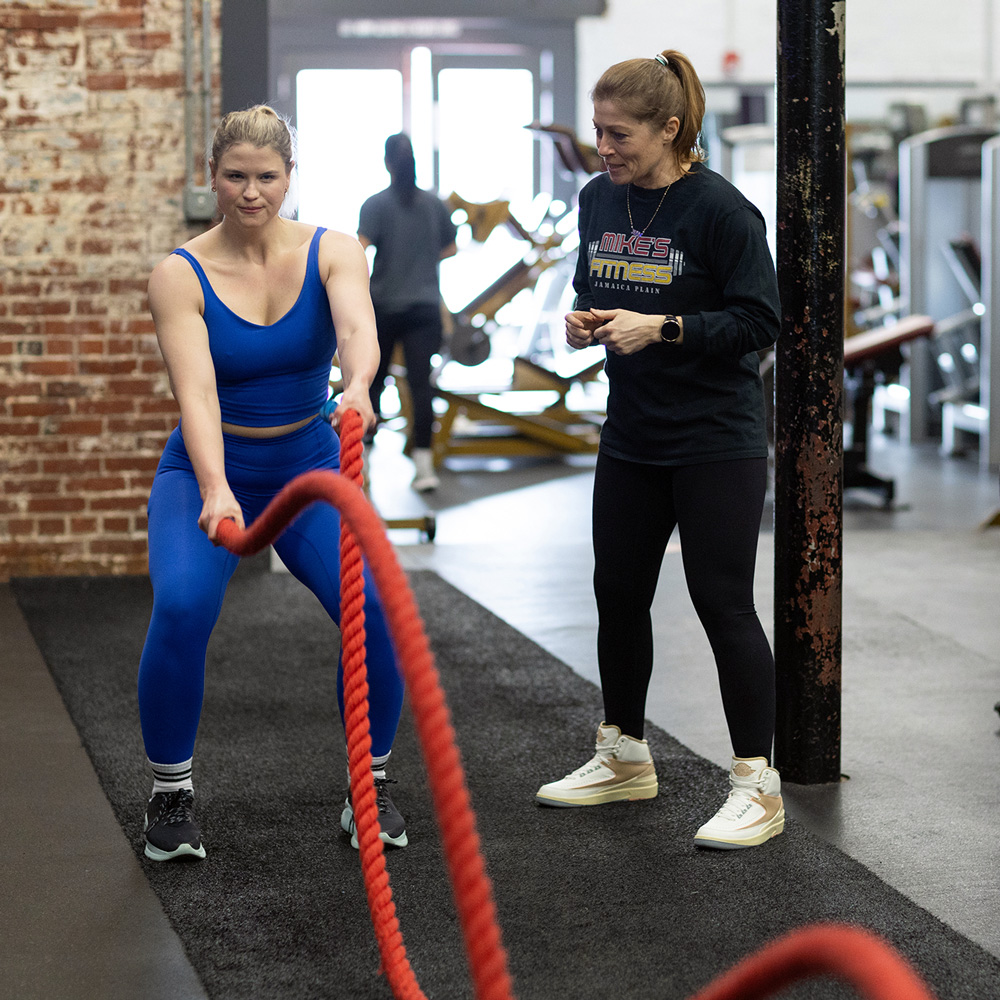 Trainer coaching member with battle ropes at a gym in Jamaica Plain.