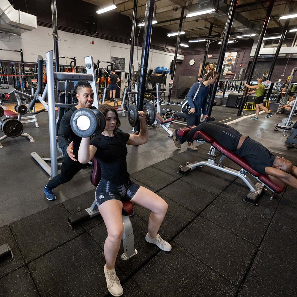 Diverse members training together with weights at a gym in Jamaica Plain.